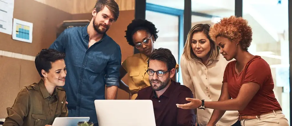 Group of colleagues crowd around laptop in discussion